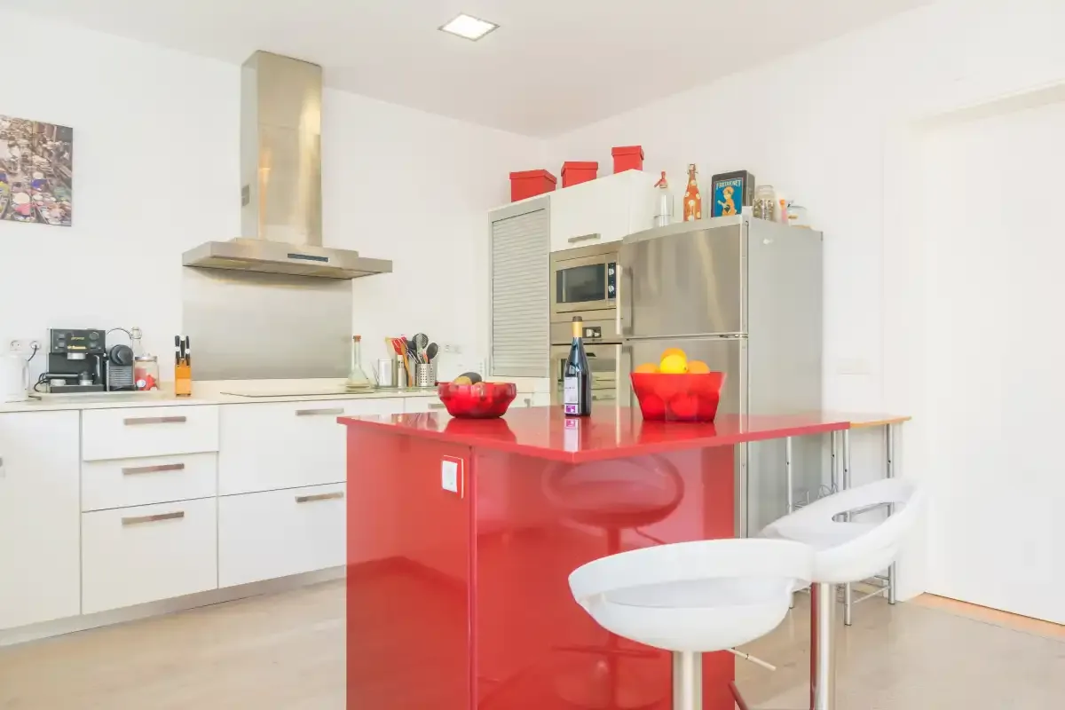 A bright kitchen with a red island and white cabinetry.