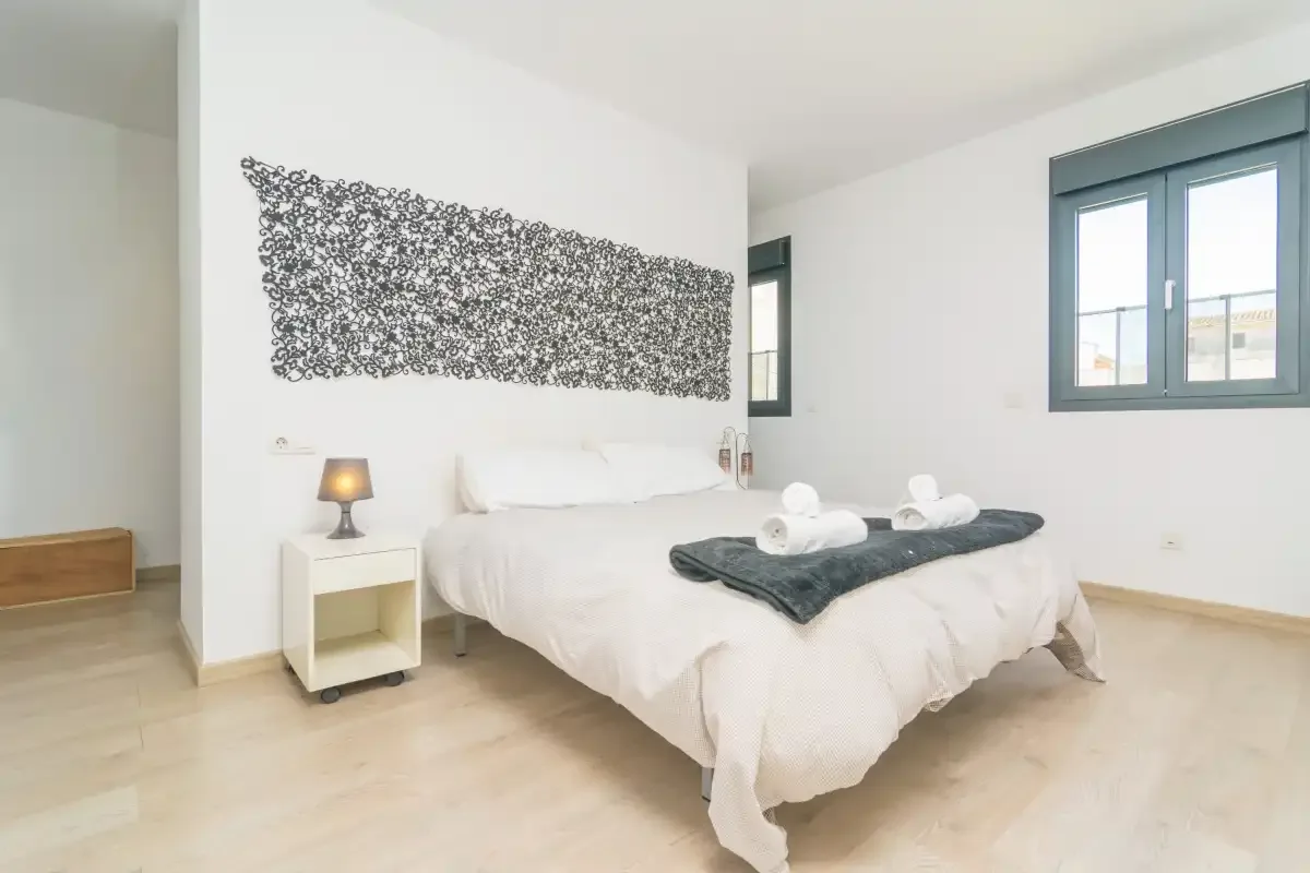 A bright bedroom with a neatly made bed and patterned wall decoration.
