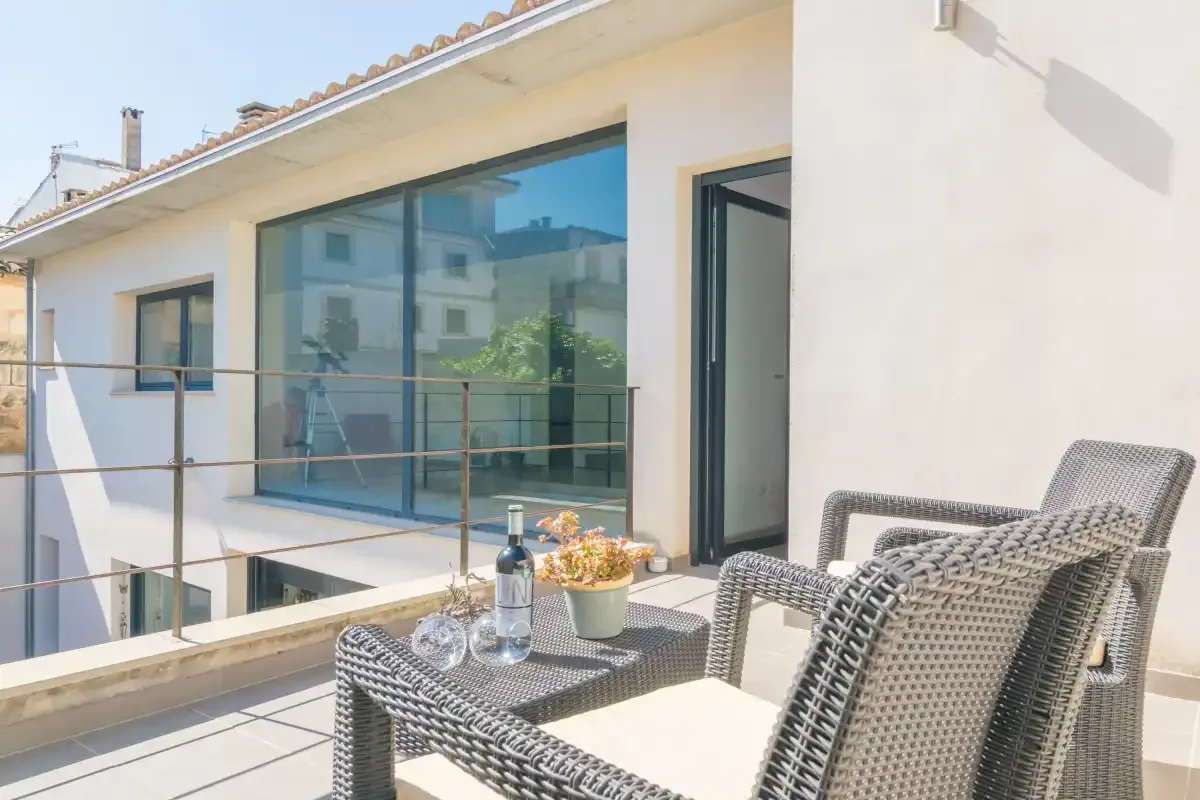 A sunlit terrace with woven seating overlooks a modern house facade.