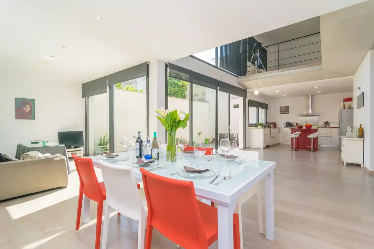 A bright open-plan dining and kitchen area with large windows and colorful chairs.