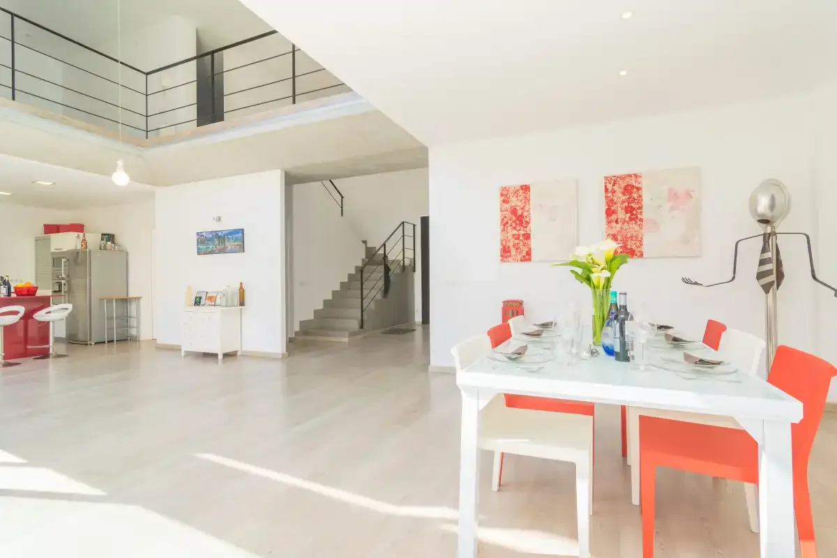 A bright open-plan dining area with a table and a staircase in the background.