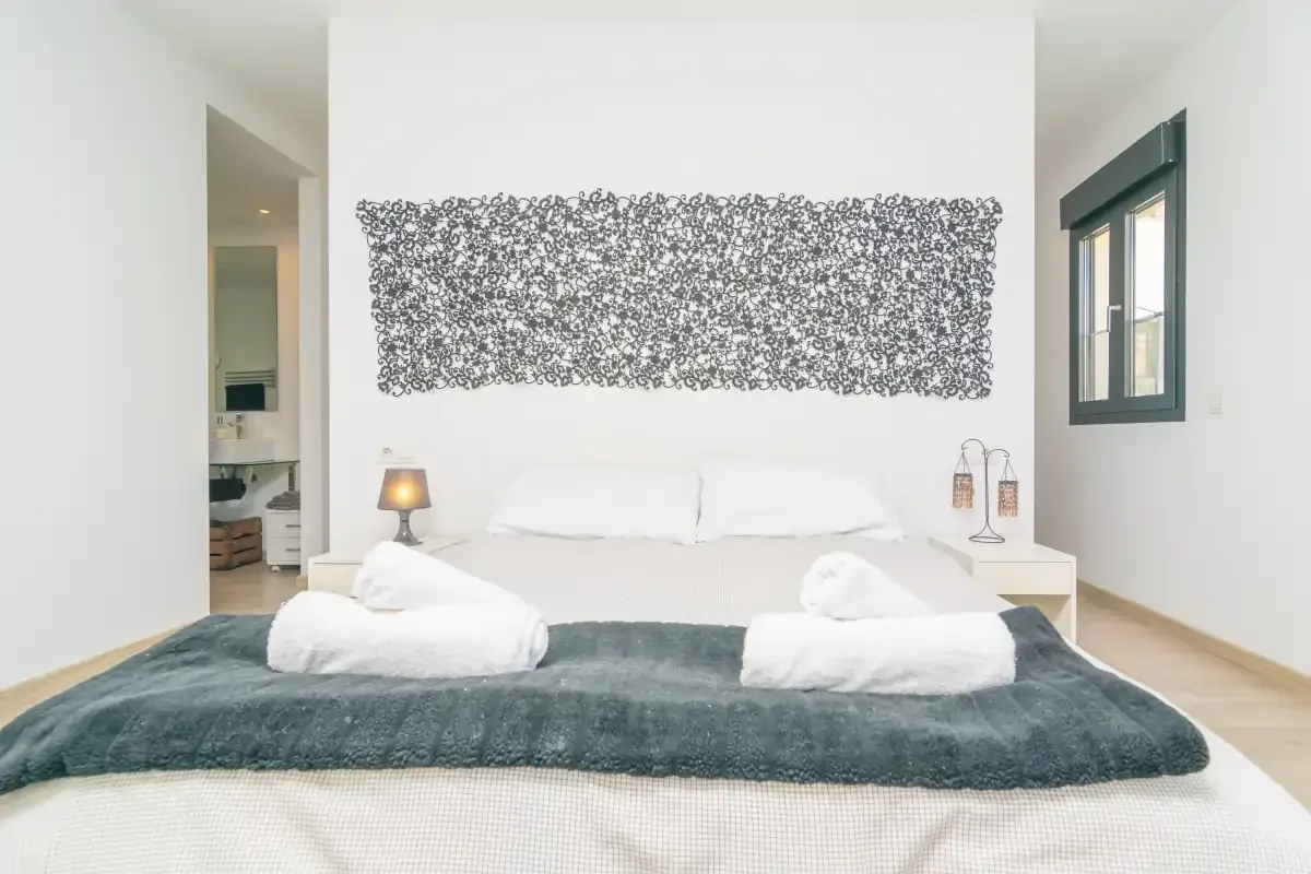 A bright bedroom features a bed with white linens and patterned wall art.