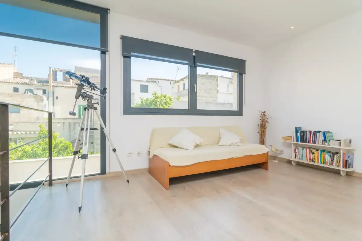 A bright bedroom with a bed, large windows, and a small bookcase.