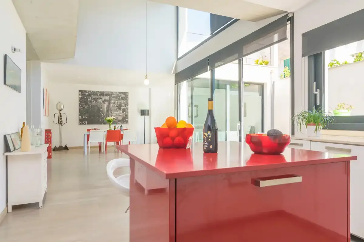 A bright kitchen and dining area with red countertops and large windows.