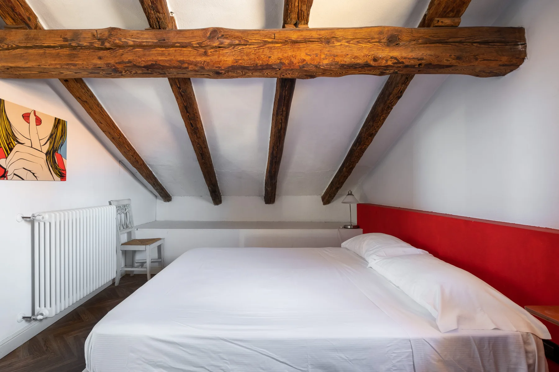 Un dormitorio con una cama bien hecha bajo vigas de madera vistas en el techo.