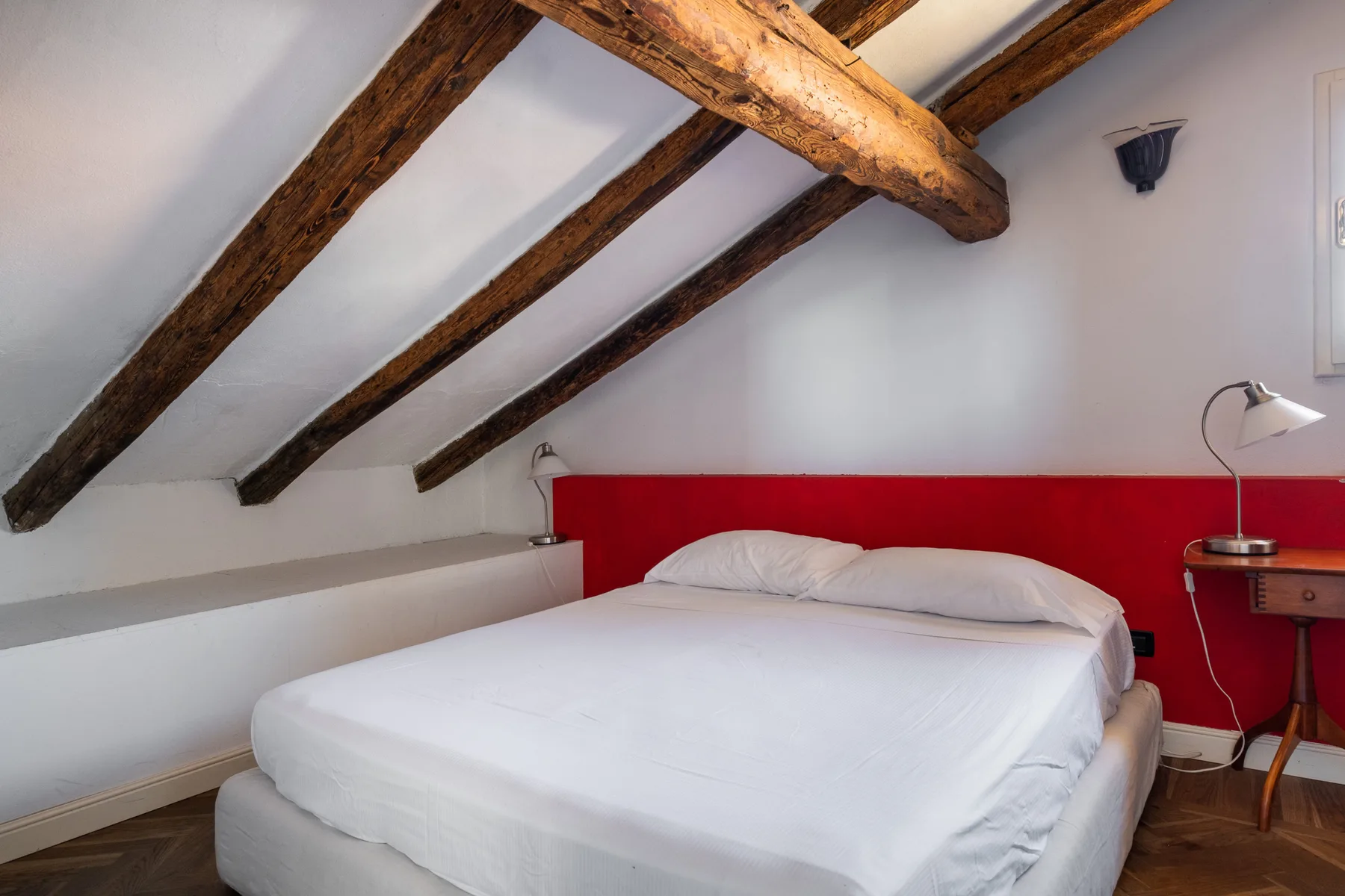 Un dormitorio con una cama blanca bajo vigas de madera vistas.