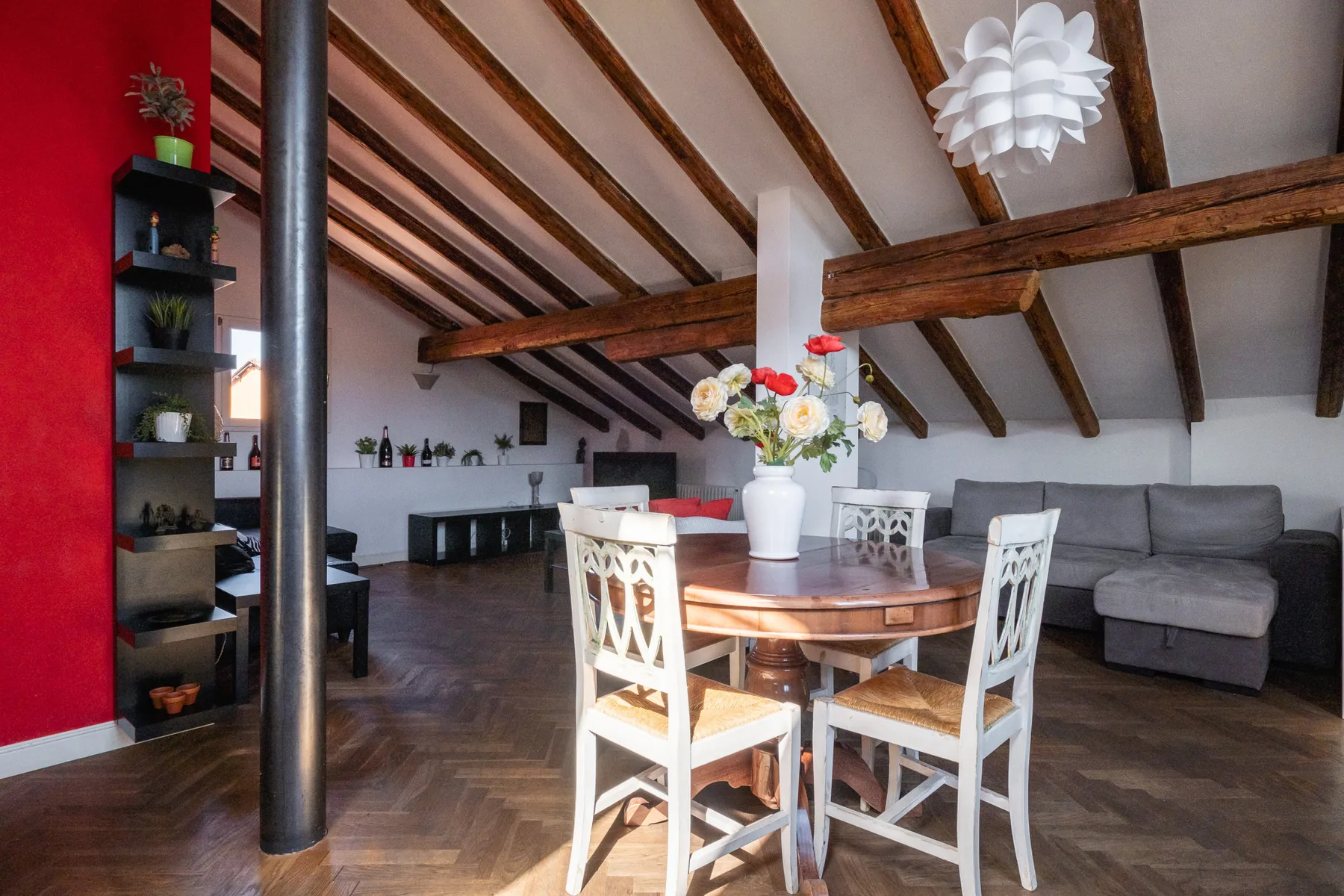 Zona de comedor y sala con mesa de madera, sillas blancas y asientos grises.