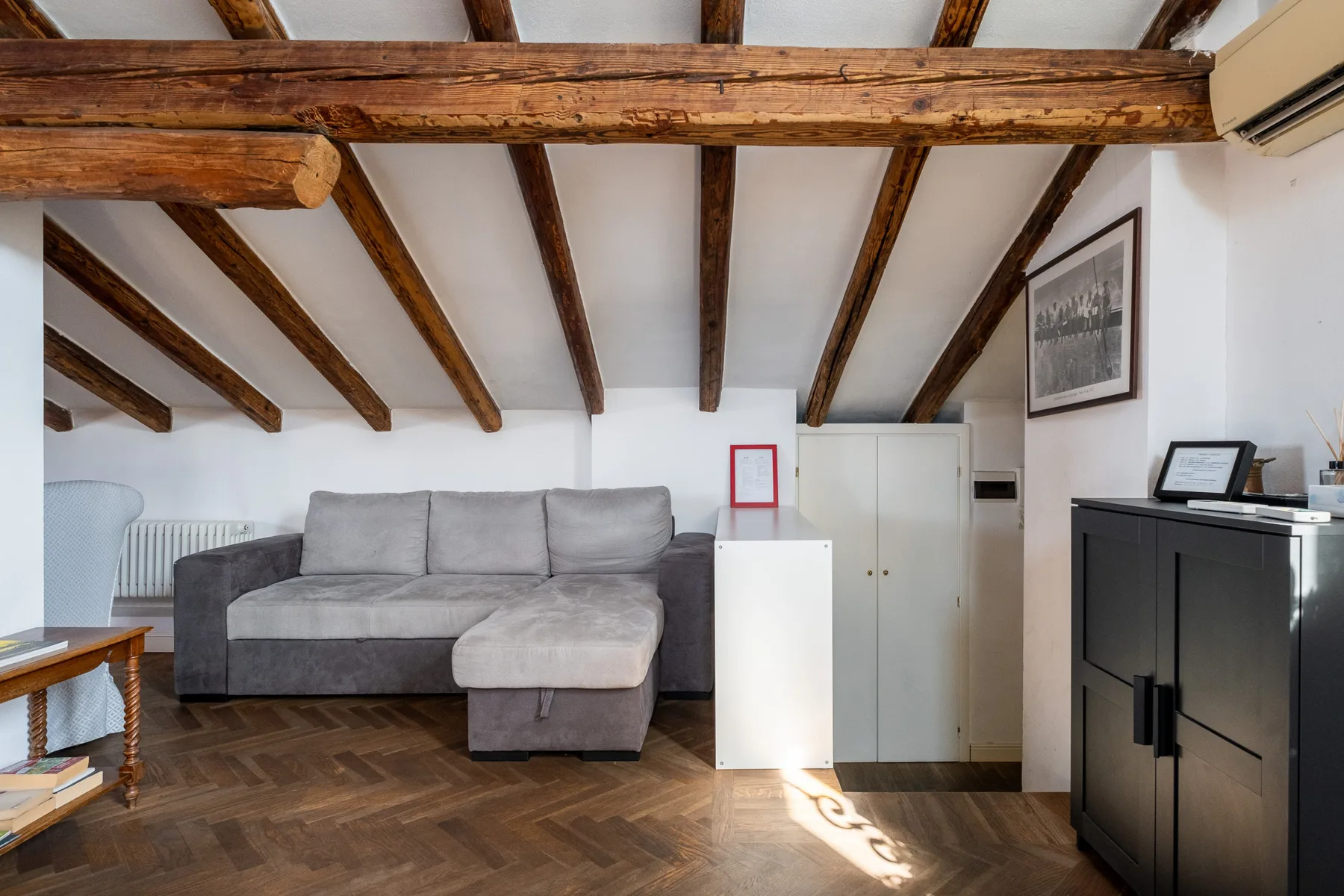 Una sala de estar con un sofá seccional gris bajo vigas de madera a la vista.