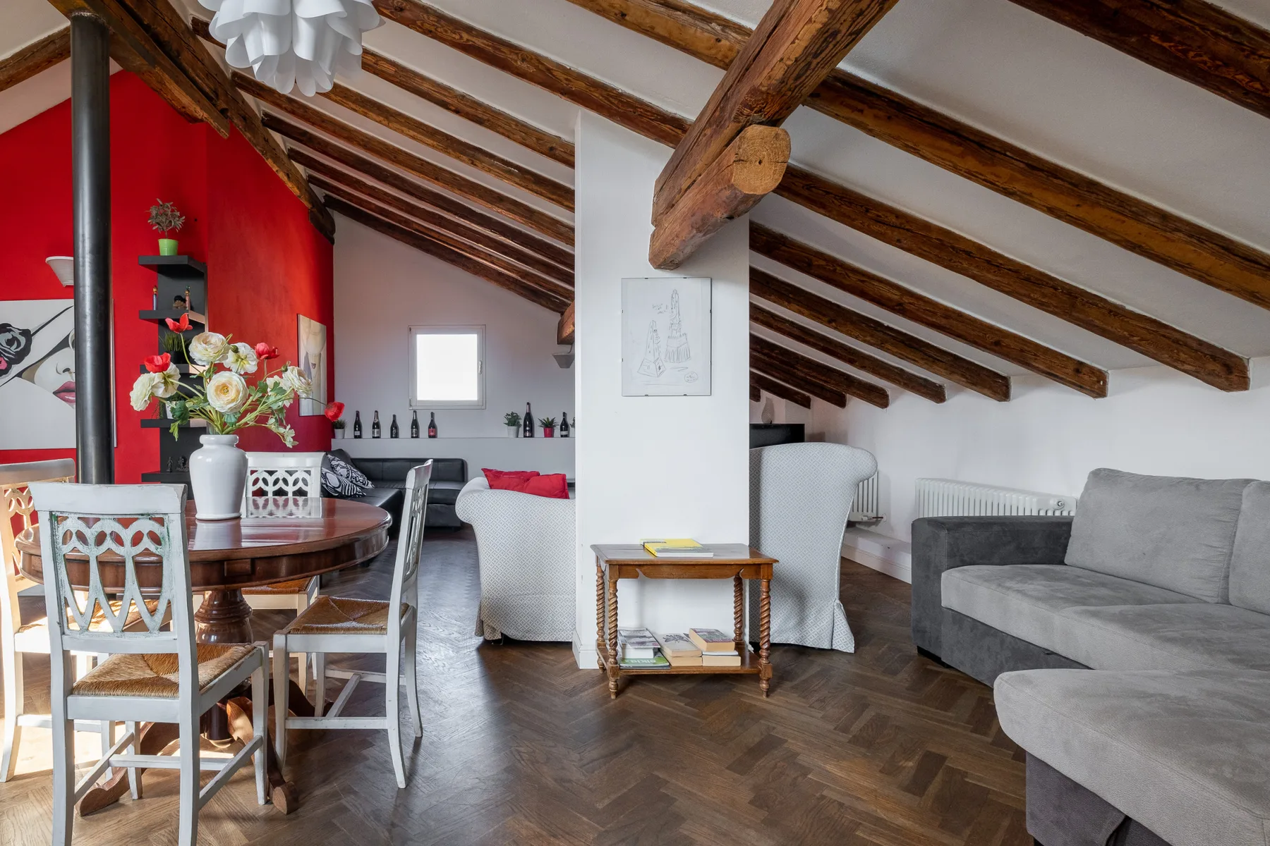 Una luminosa sala de estar y comedor tiene una mesa y asientos grises bajo vigas expuestas.
