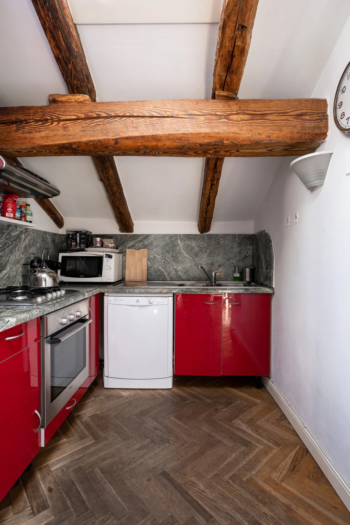 Una cocina pequeña con gabinetes rojos, microondas y vigas de madera expuestas en el techo.