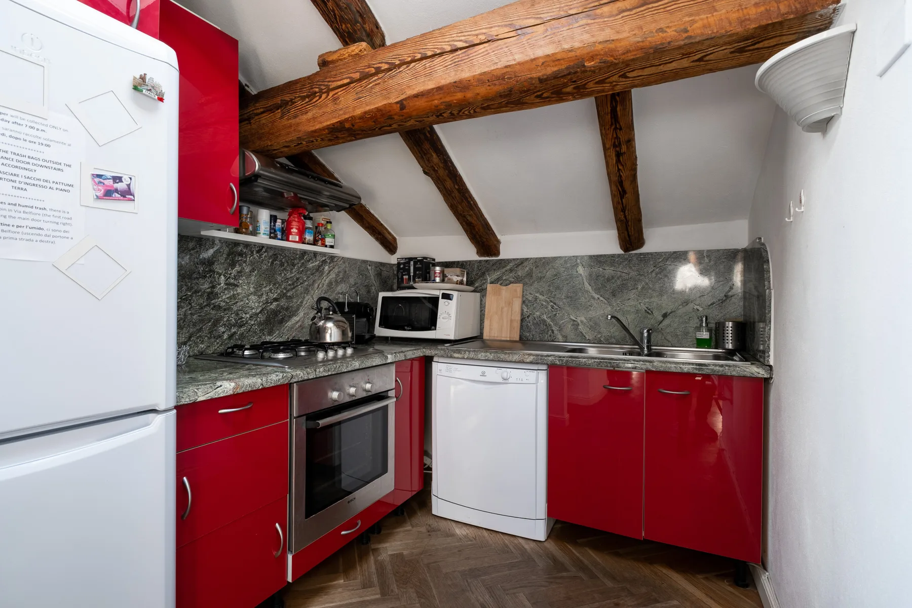 Una cocina compacta con gabinetes rojos, un refrigerador y vigas de madera expuestas.