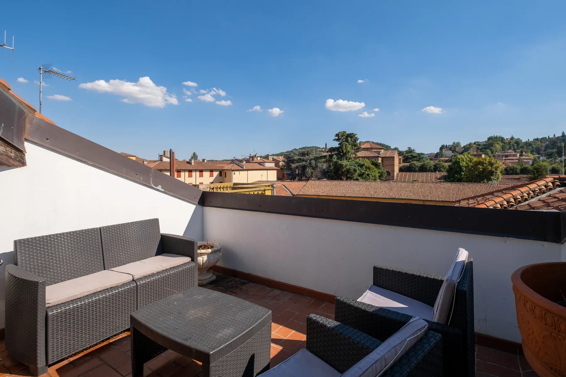 Una terraza en la azotea con asientos al aire libre mira hacia edificios cercanos y una colina arbolada.