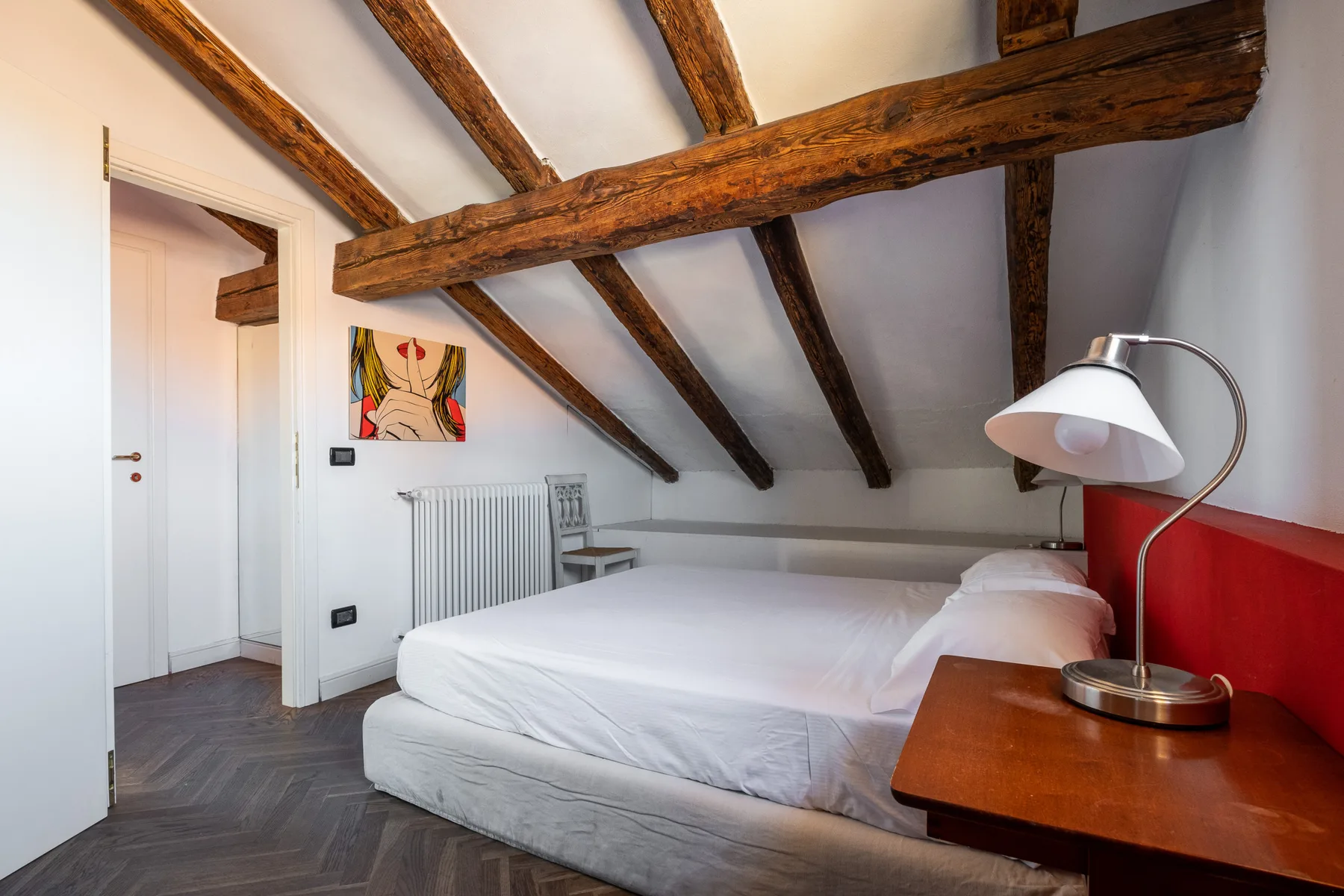 Un dormitorio con una cama, vigas de madera expuestas en el techo y una lámpara de mesita.