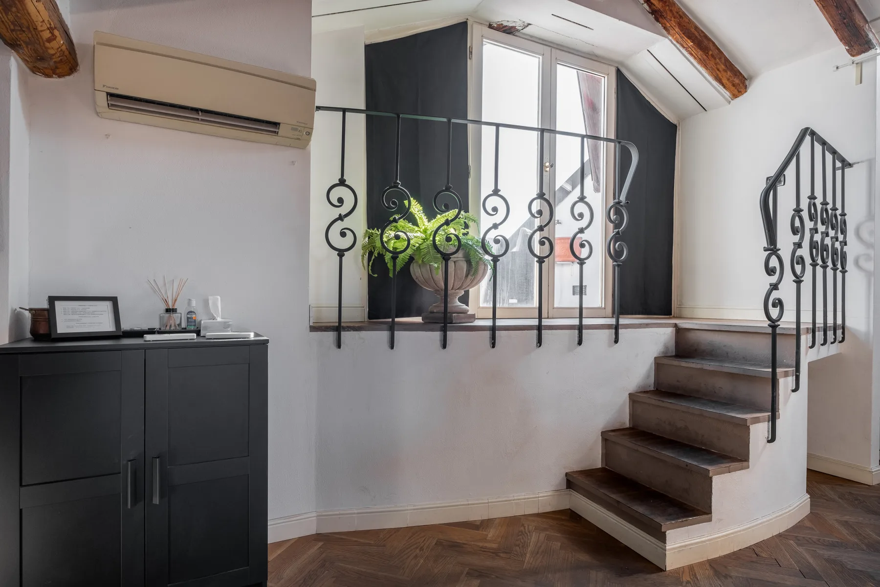 Un interior tipo loft con una escalera, una barandilla decorativa y una ventana.