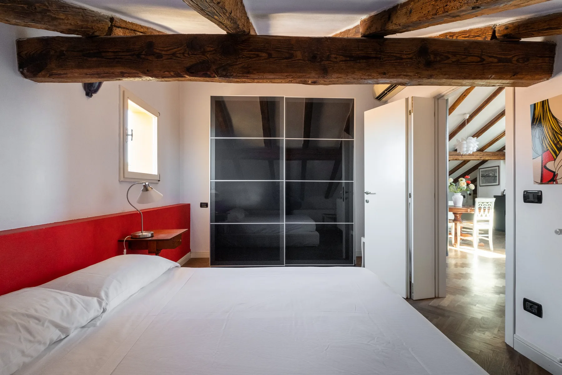 Un dormitorio con una cama, puertas correderas oscuras y vigas de madera vistas.