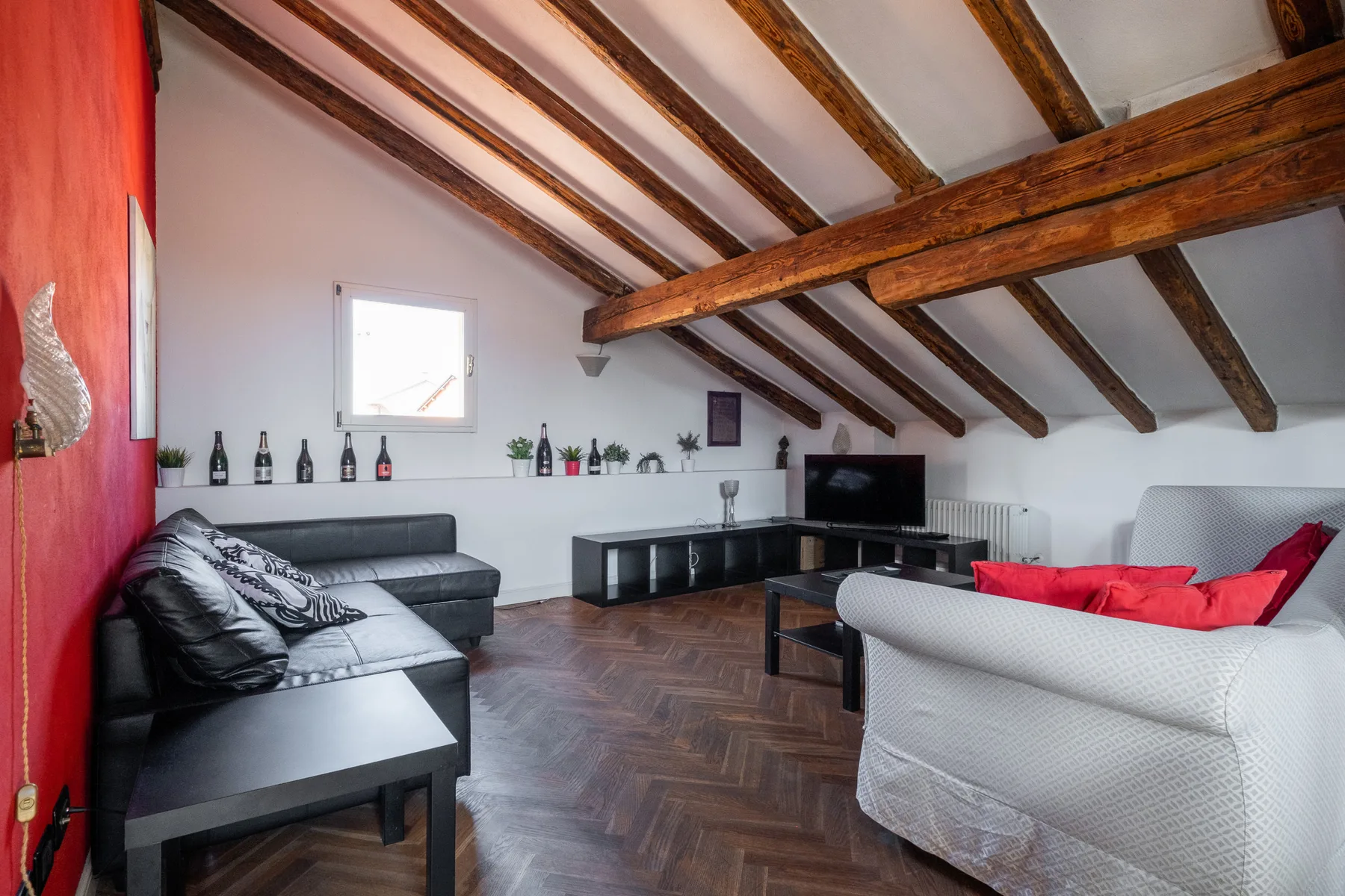 Una sala de estar con asientos, un televisor y vigas de madera expuestas en el techo.