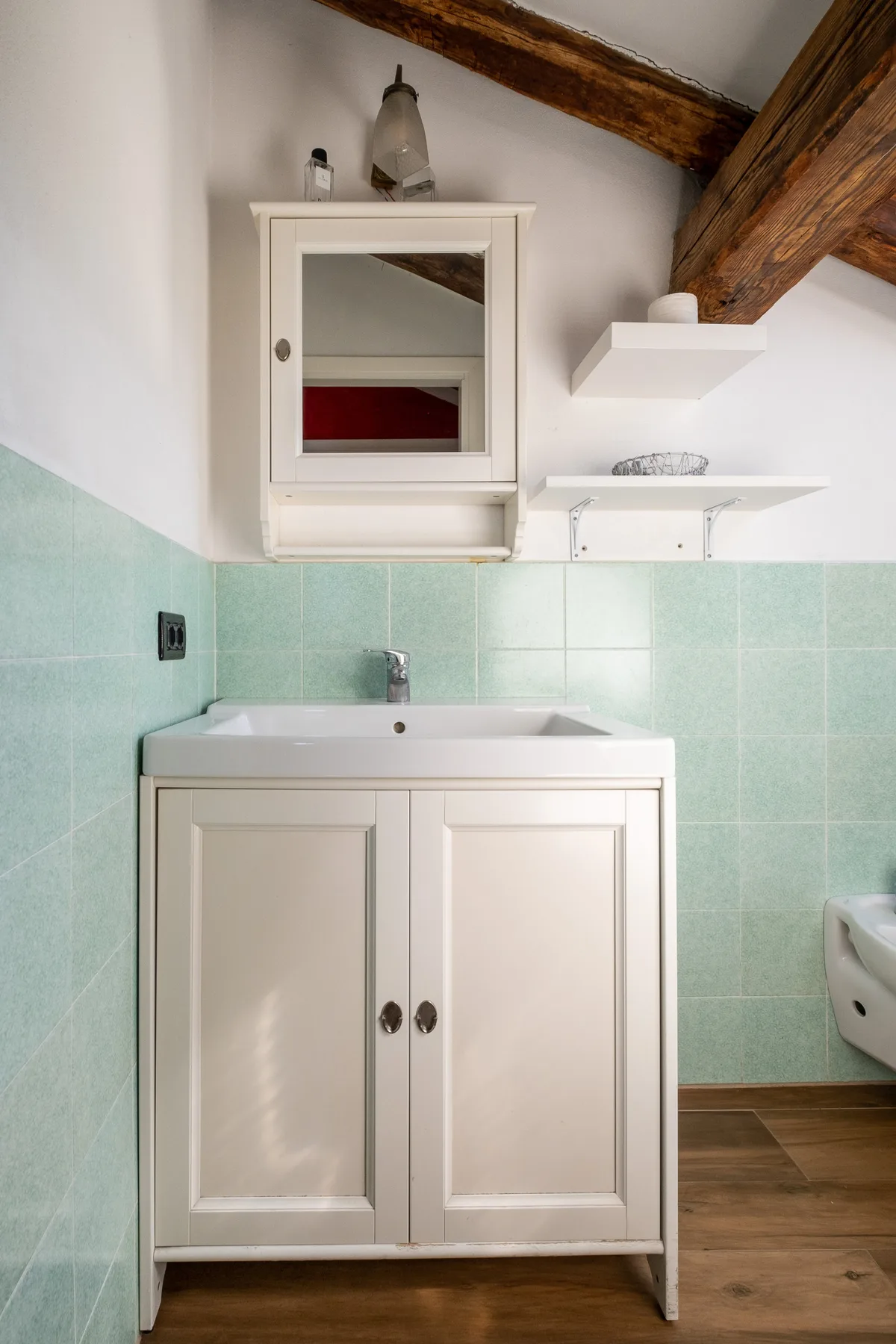 Un mueble de baño con espejo está junto a paredes de azulejos verde claro.