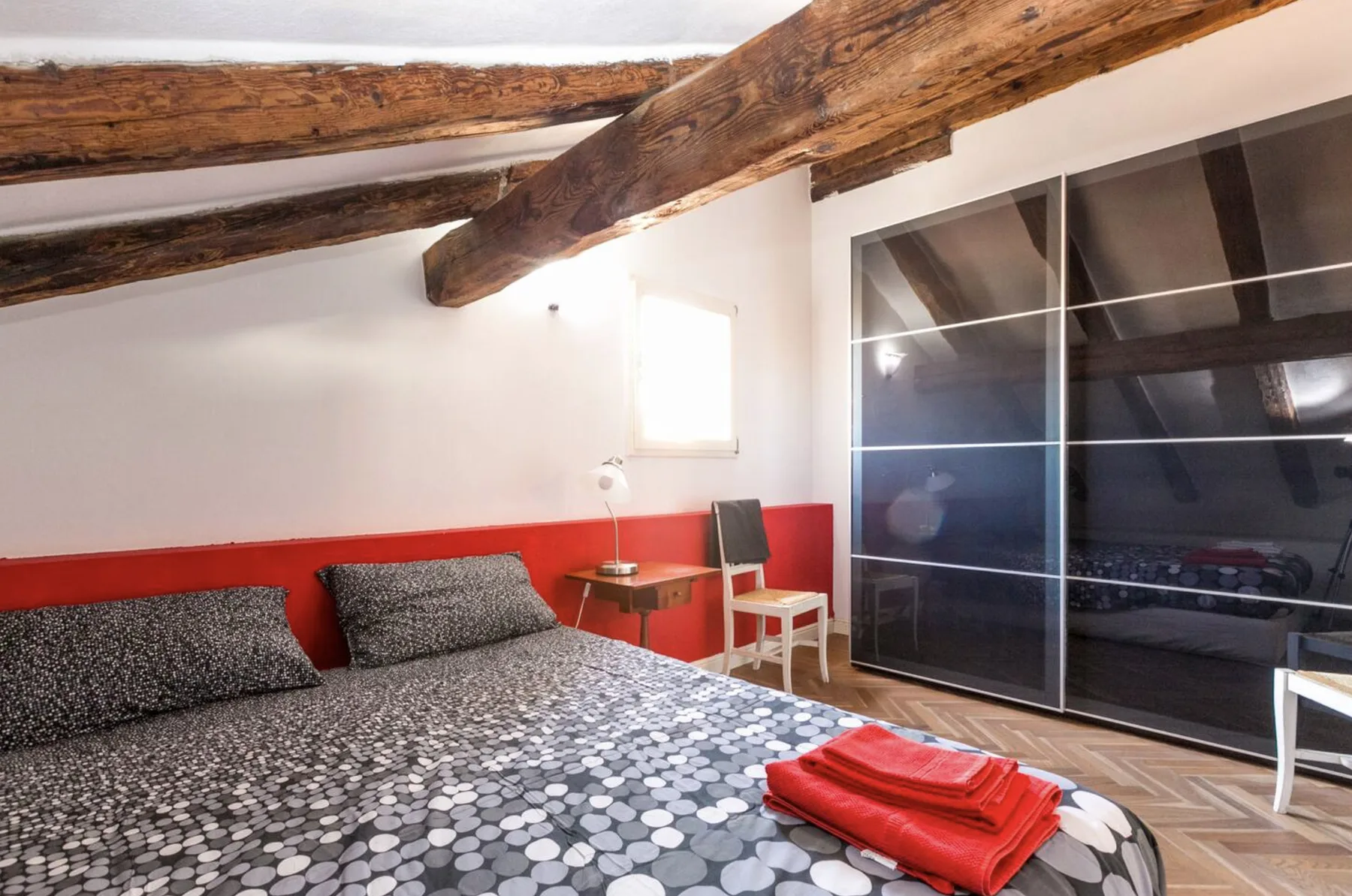 Un dormitorio con ropa de cama estampada, vigas de madera vistas y un armario corredero grande.