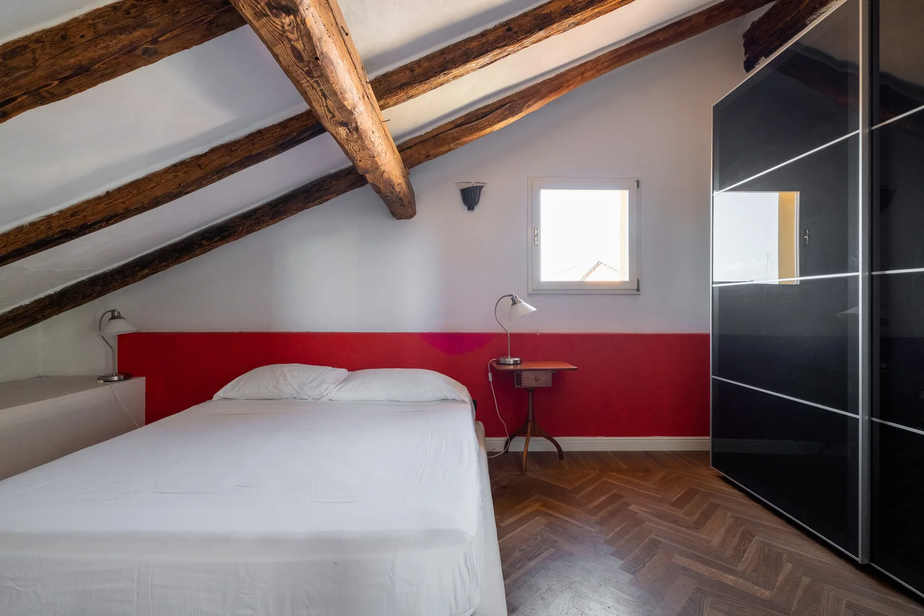 Un dormitorio con una cama blanca bajo vigas de madera expuestas.
