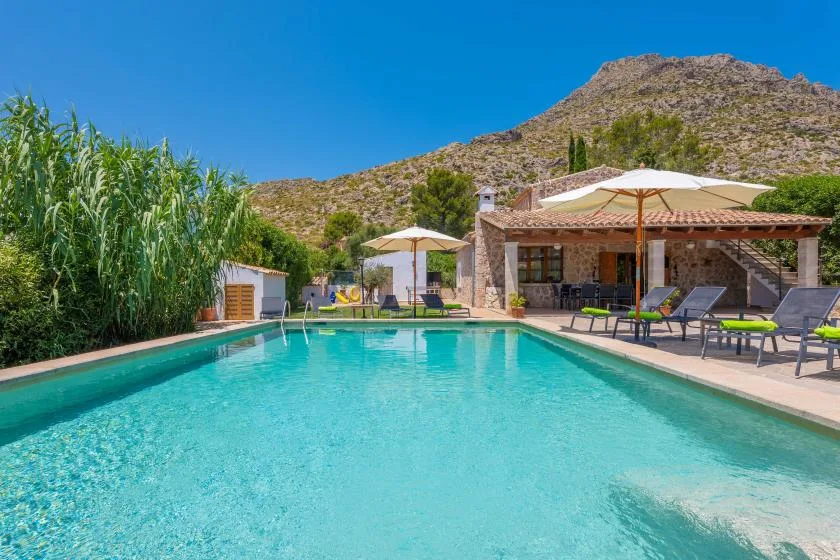 An outdoor swimming pool beside a patio with lounge seating and a mountain backdrop.
