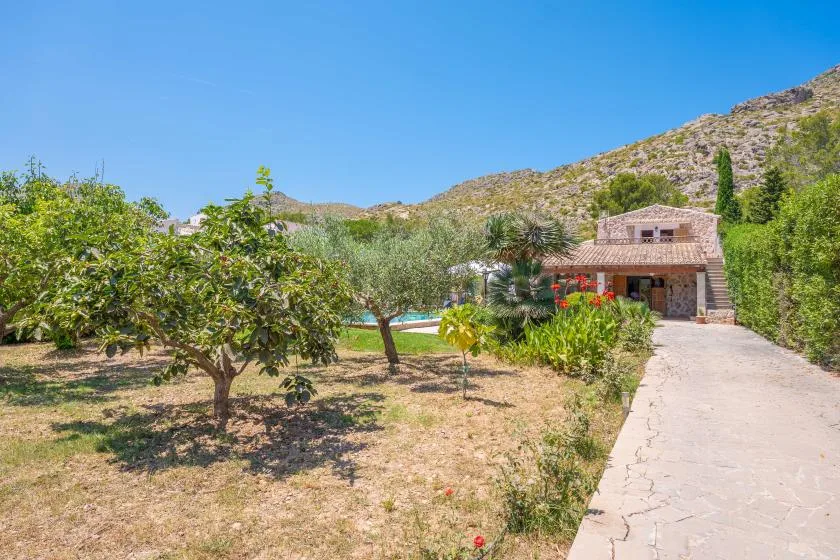 A garden path leads to a stone house among trees and flowering plants.