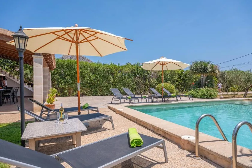 Outdoor swimming pool beside a sunny patio with loungers and large umbrellas.