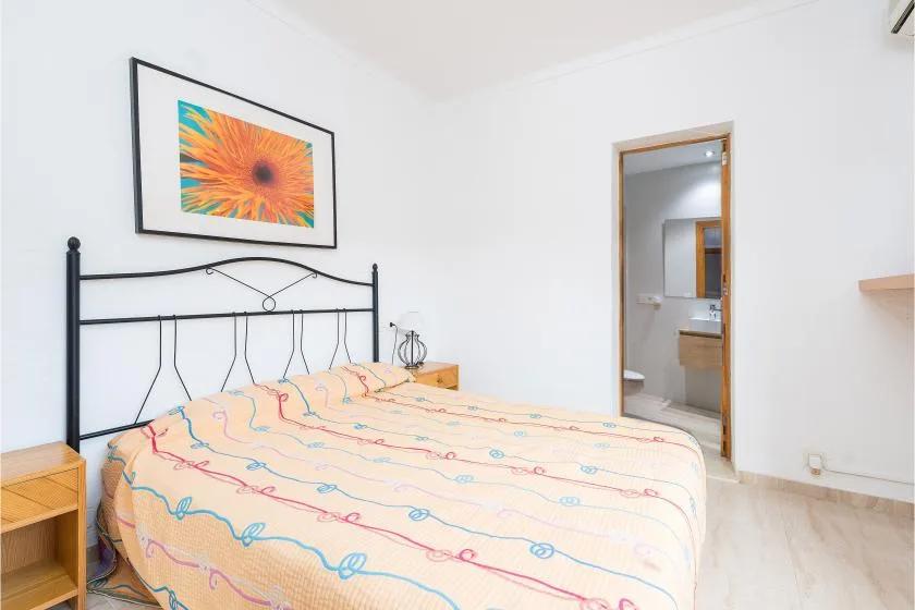 A bedroom with a bed beneath framed floral artwork and an open doorway.