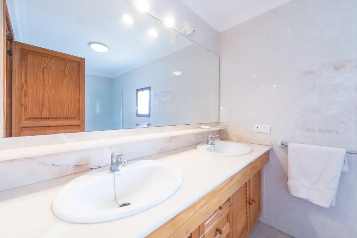 A bright bathroom with a long vanity, two sinks, and a large mirror.