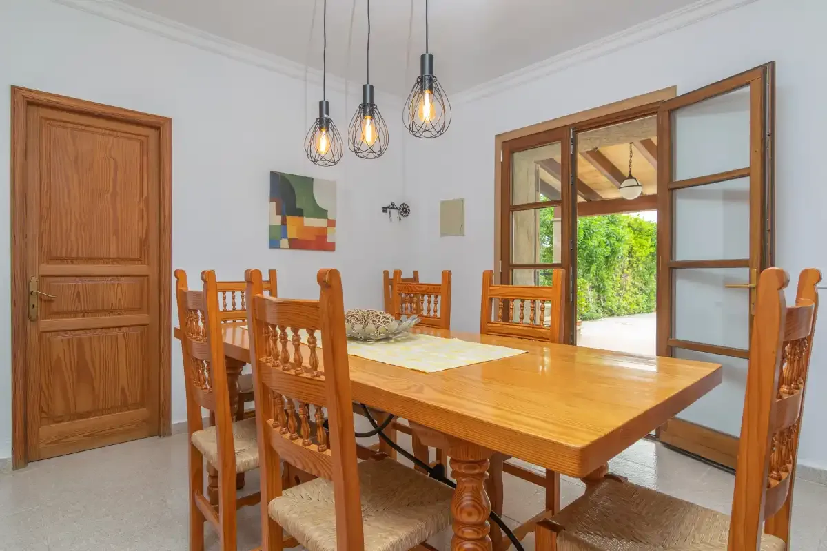A dining room with a wooden table and chairs beside open glass doors.
