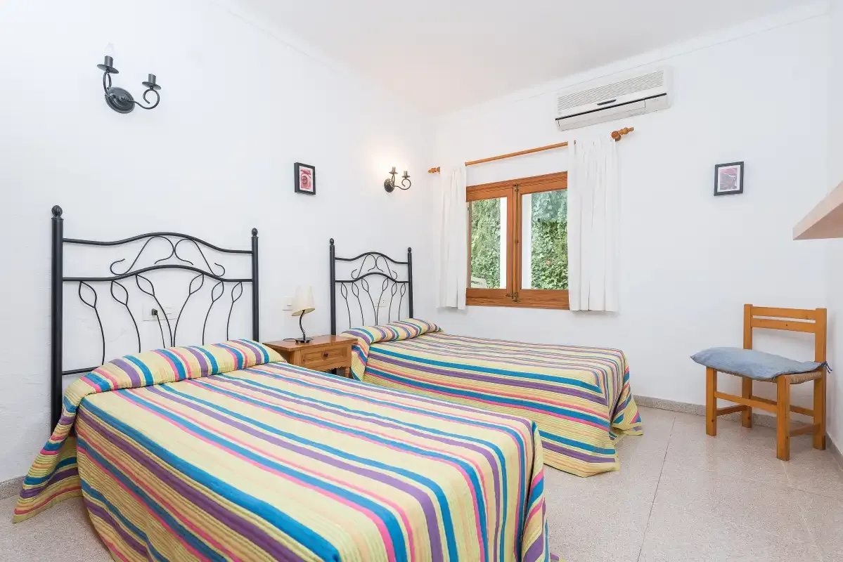 A bright bedroom with two beds covered in colorful striped bedding.