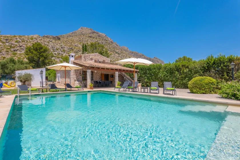 An outdoor swimming pool sits beside a shaded patio, with a mountain in the background.