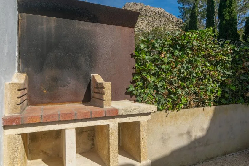 An outdoor masonry barbecue sits beside a leafy hedge.