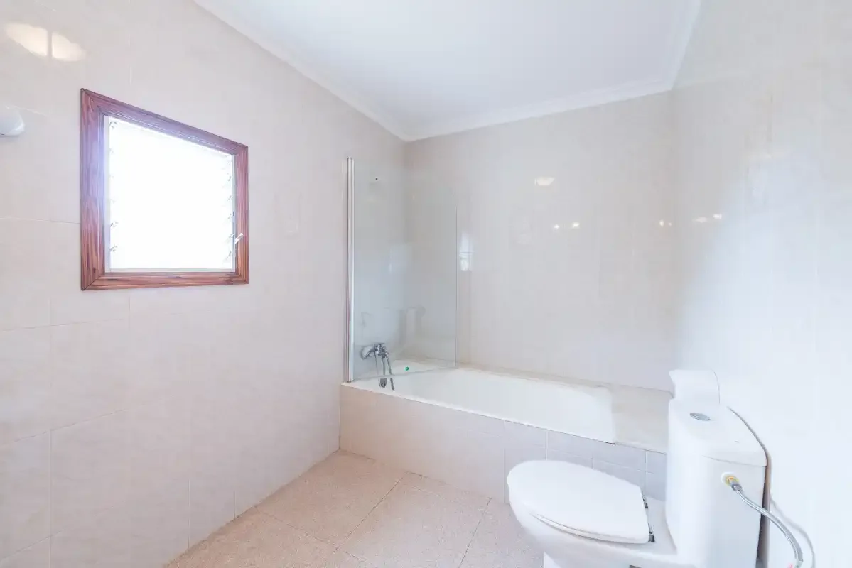A bright bathroom with a bathtub, toilet, and window.