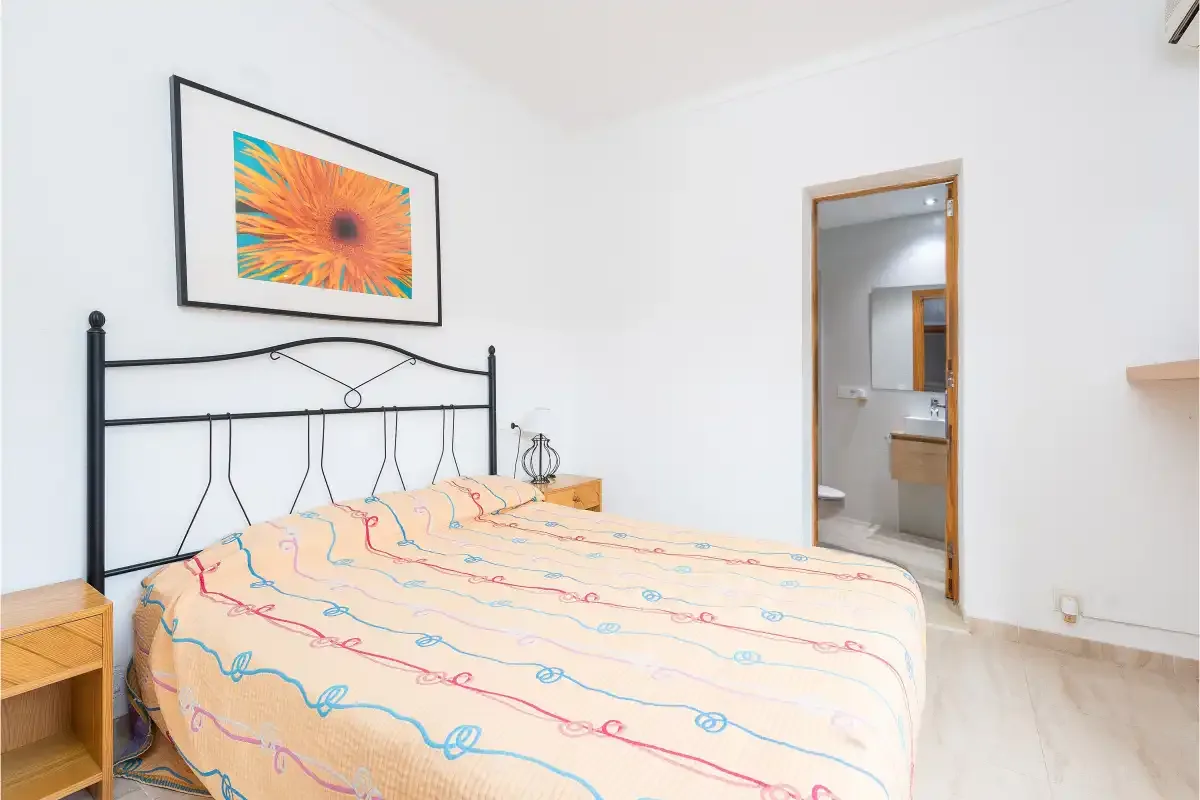 A bedroom with a bed beneath framed artwork and an open doorway.