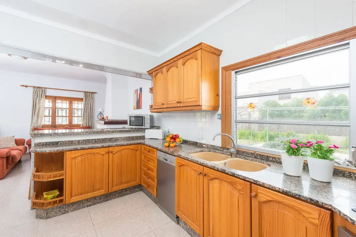 A bright kitchen with wooden cabinets, stone counters, and a large window.