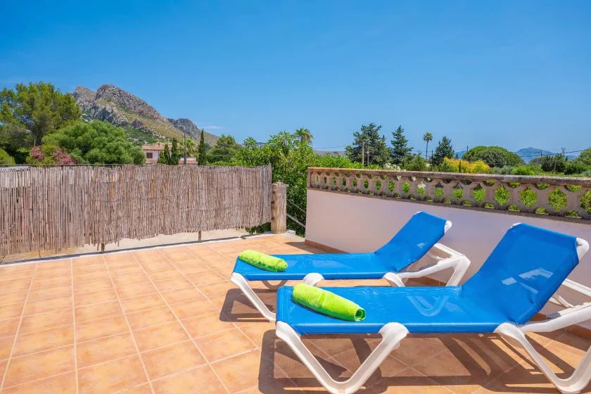 A sunny rooftop terrace with blue lounge chairs and mountain views.