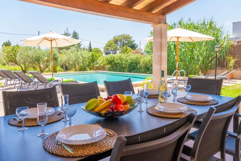 A shaded outdoor dining area overlooks a swimming pool and garden.