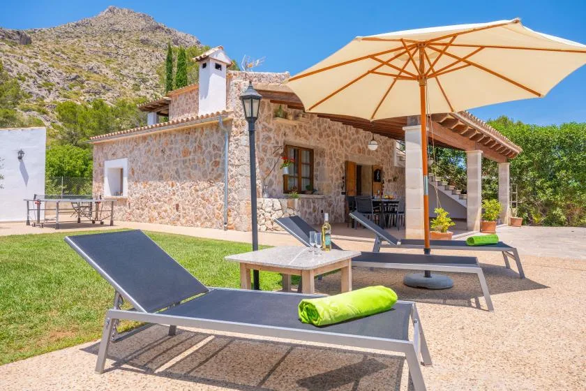 A sunny stone house patio with lounge seating beneath a large umbrella.