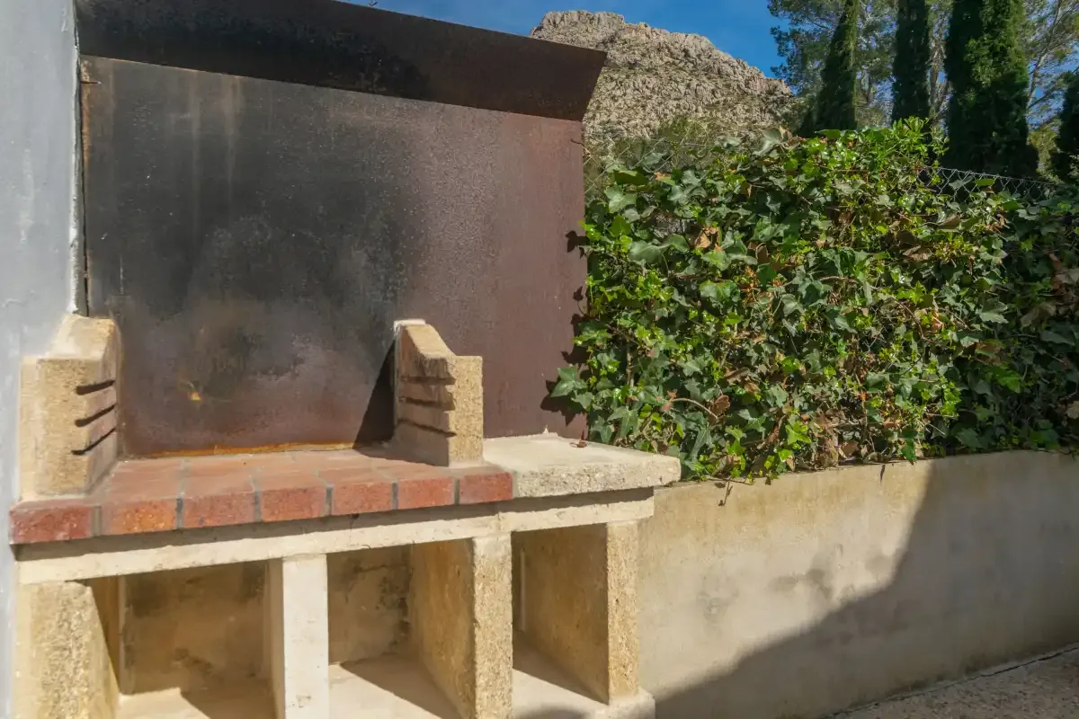 An outdoor masonry barbecue stands beside a leafy garden wall.