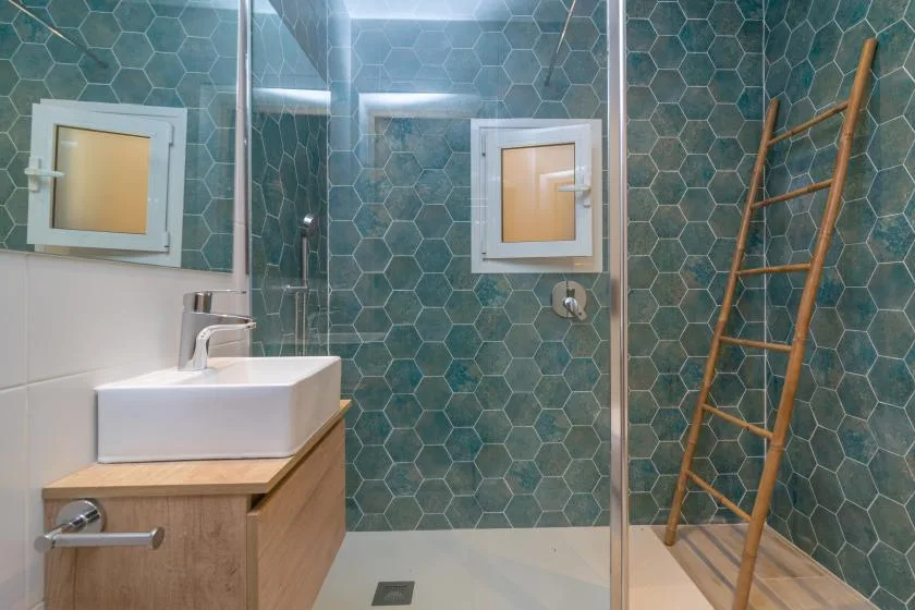 A tiled bathroom with a sink, shower, and wooden ladder.