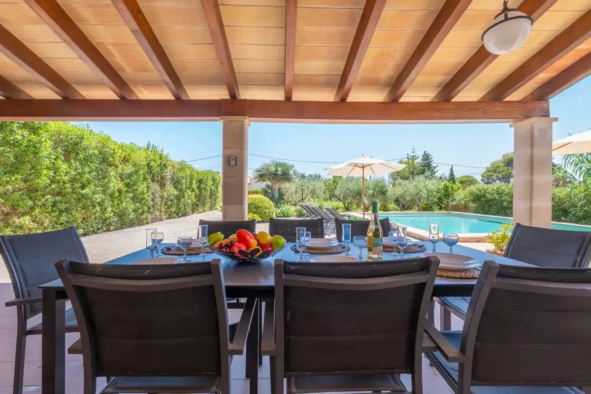 A covered outdoor dining area overlooks a swimming pool and garden.