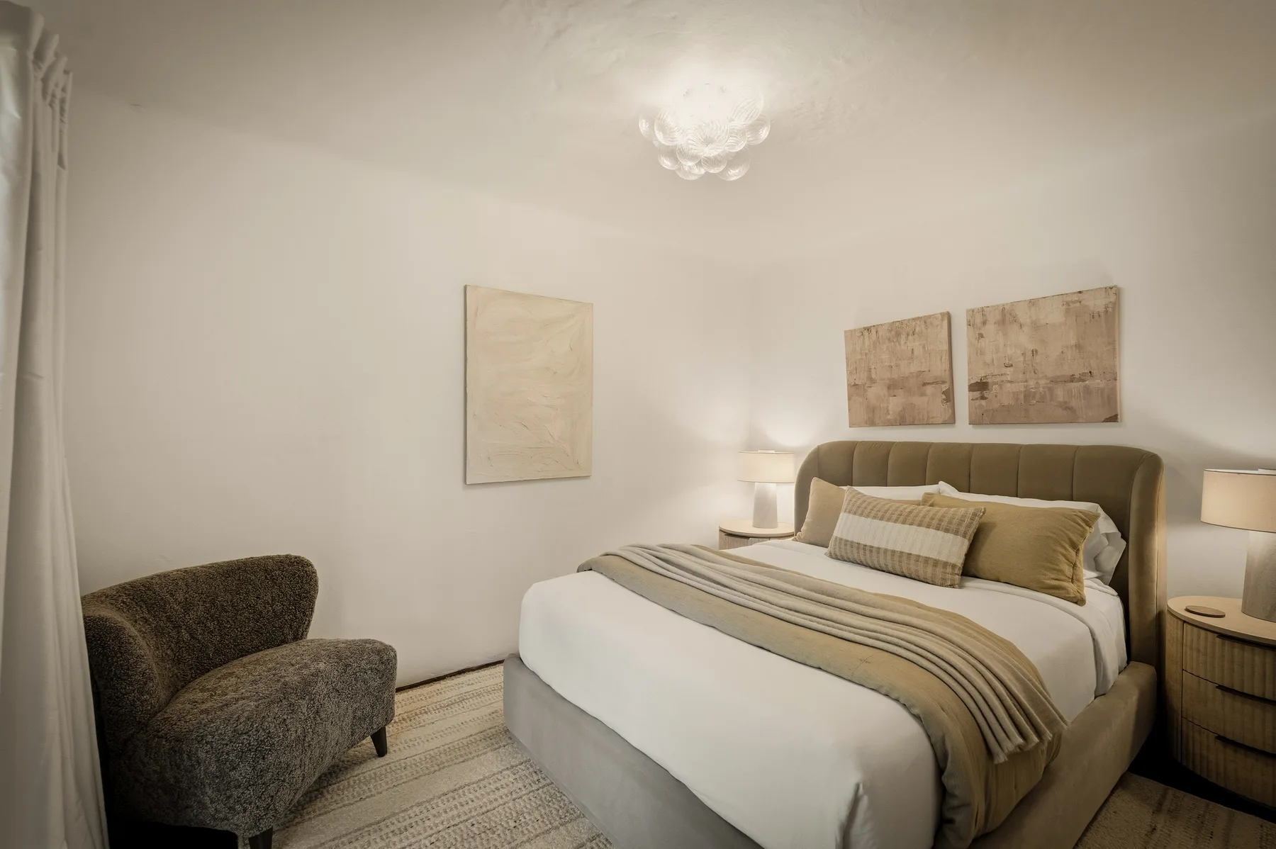 Un dormitorio con una cama bien tendida y cuadros en la pared.