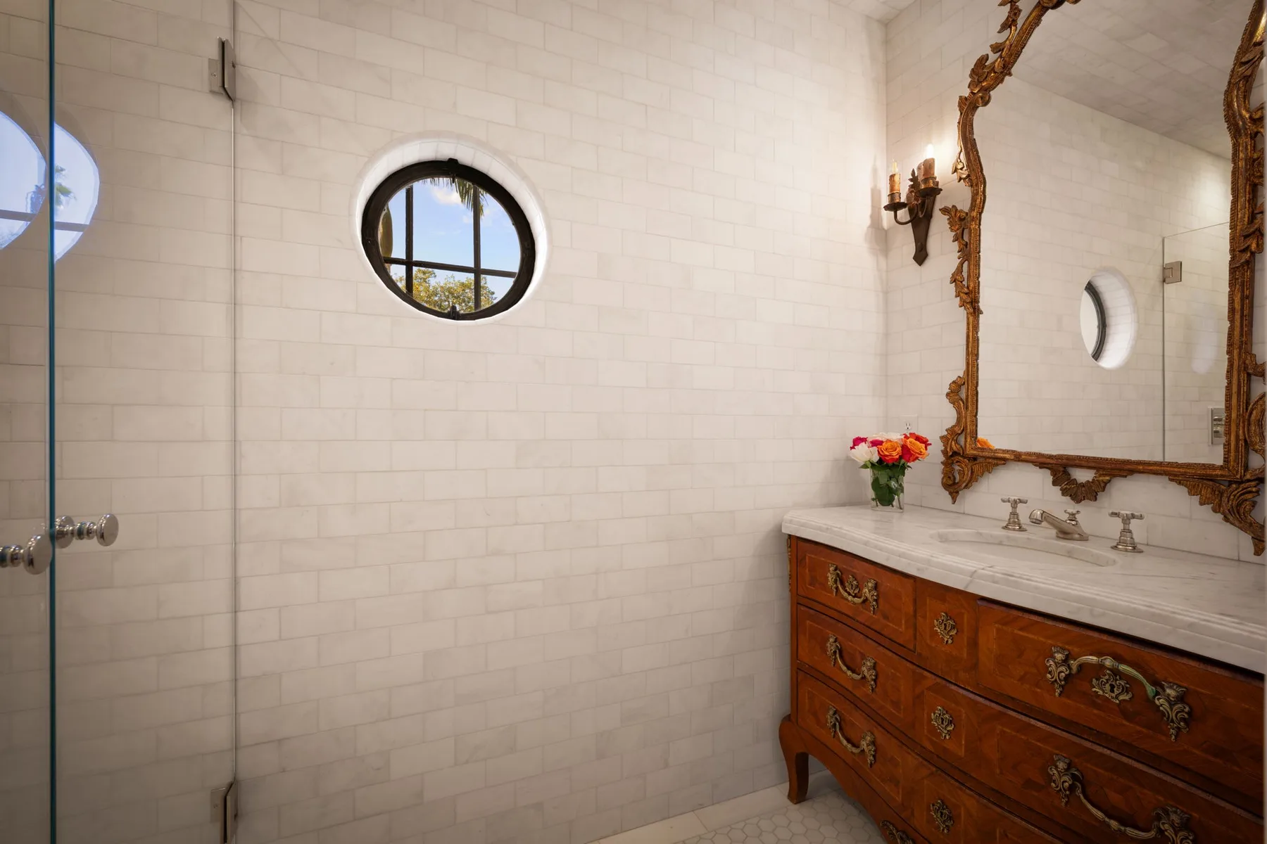 Un baño alicatado con un mueble de madera y una ventana redonda.
