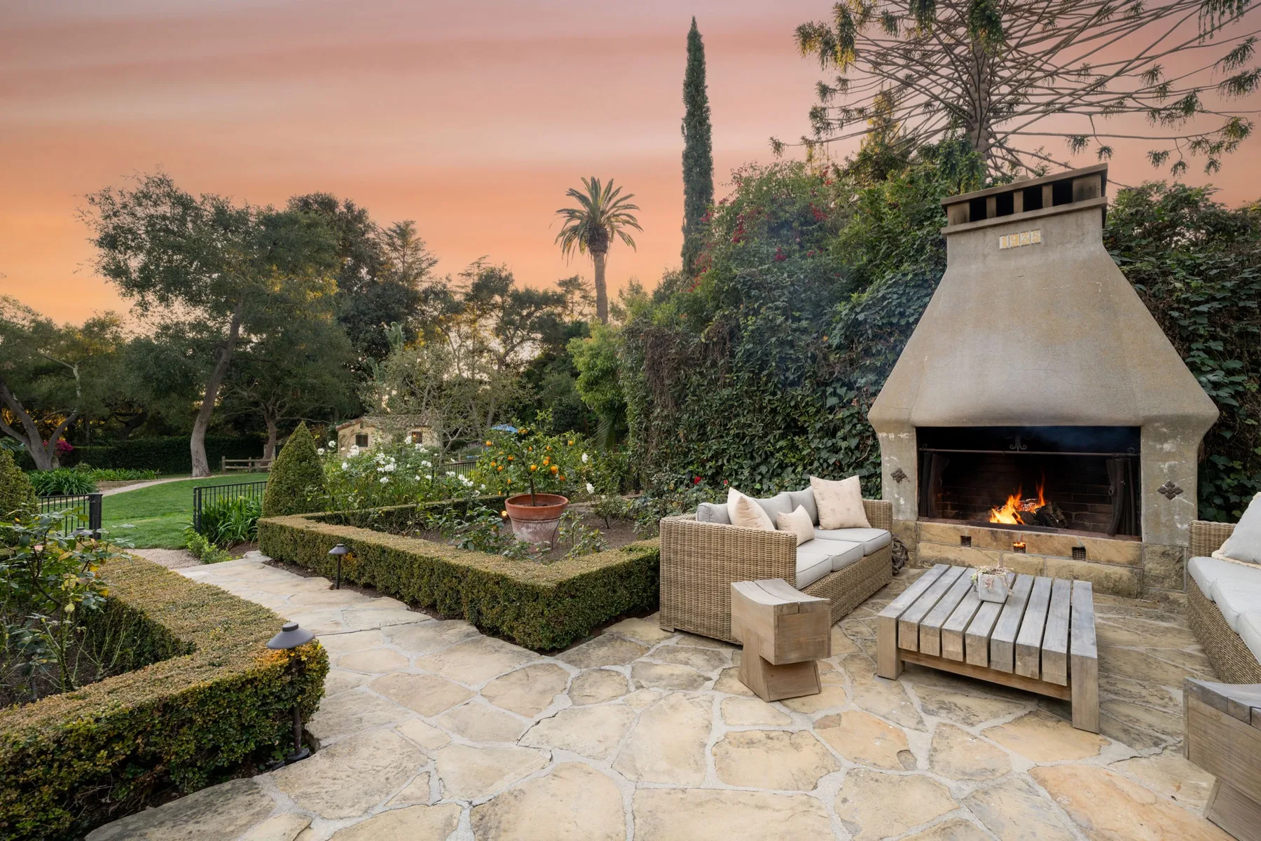 Un patio ajardinado con asientos al aire libre y una chimenea encendida al atardecer.