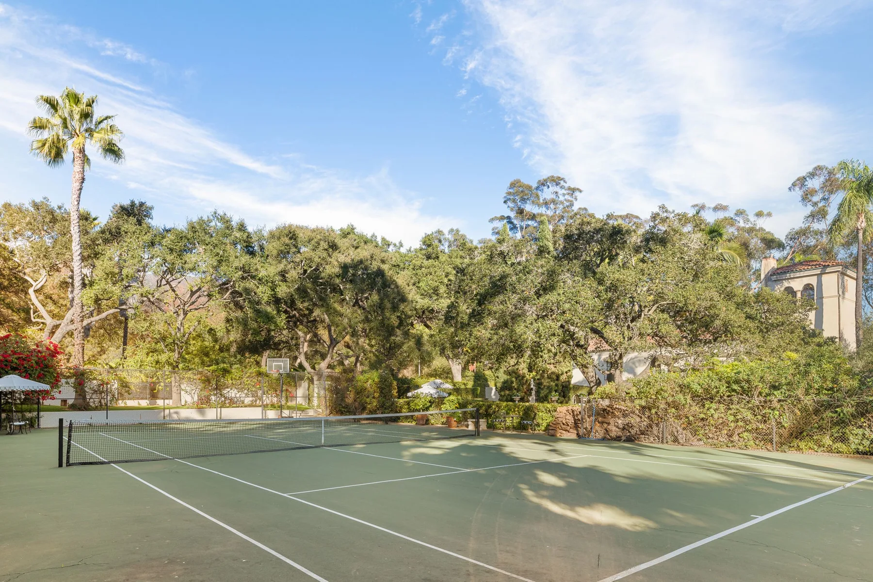 Una cancha de tenis al aire libre está rodeada de árboles bajo un cielo azul.