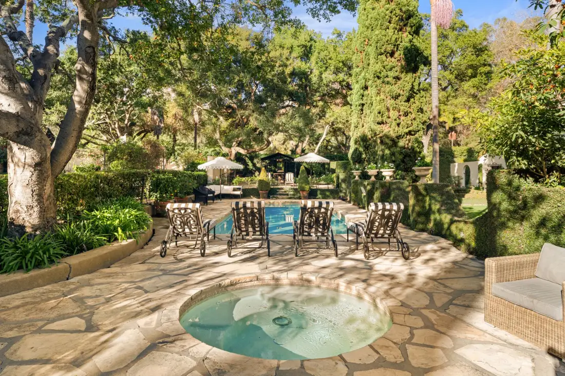 Una zona ajardinada con piscina al aire libre, un pequeño spa circular y asientos.
