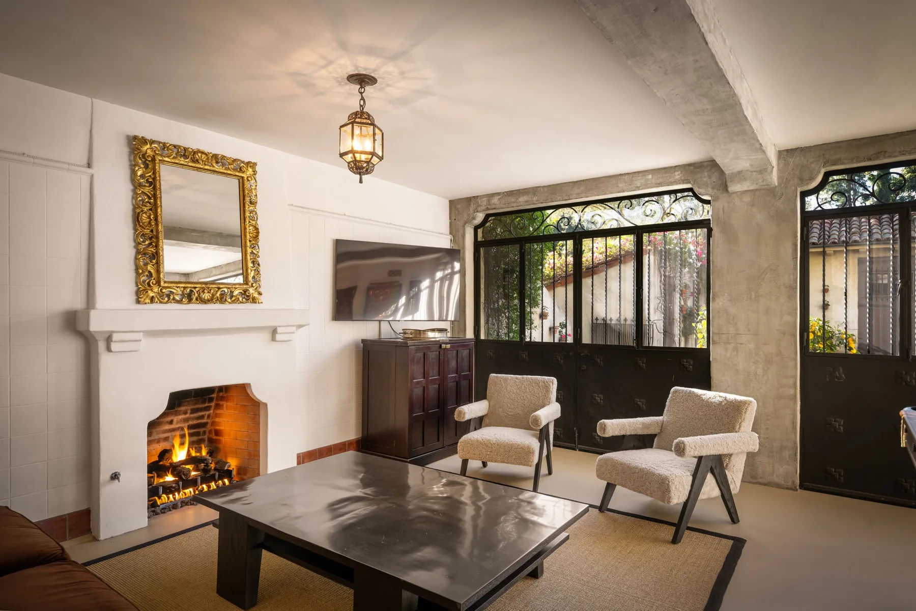 Una sala de estar con chimenea, mesa de centro y asientos junto a grandes ventanas.