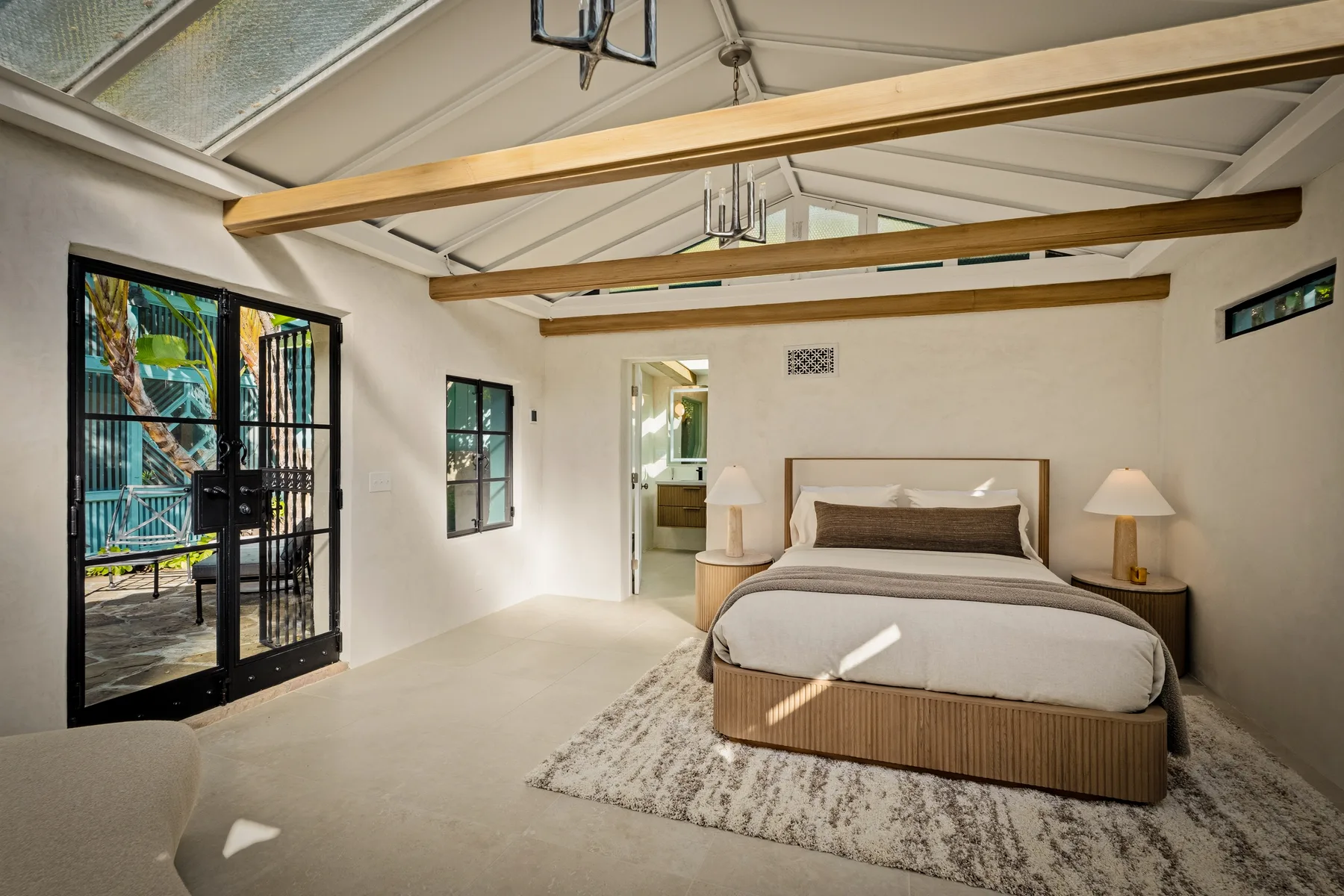 Un dormitorio luminoso con una cama bajo vigas de madera vistas y puertas de cristal.