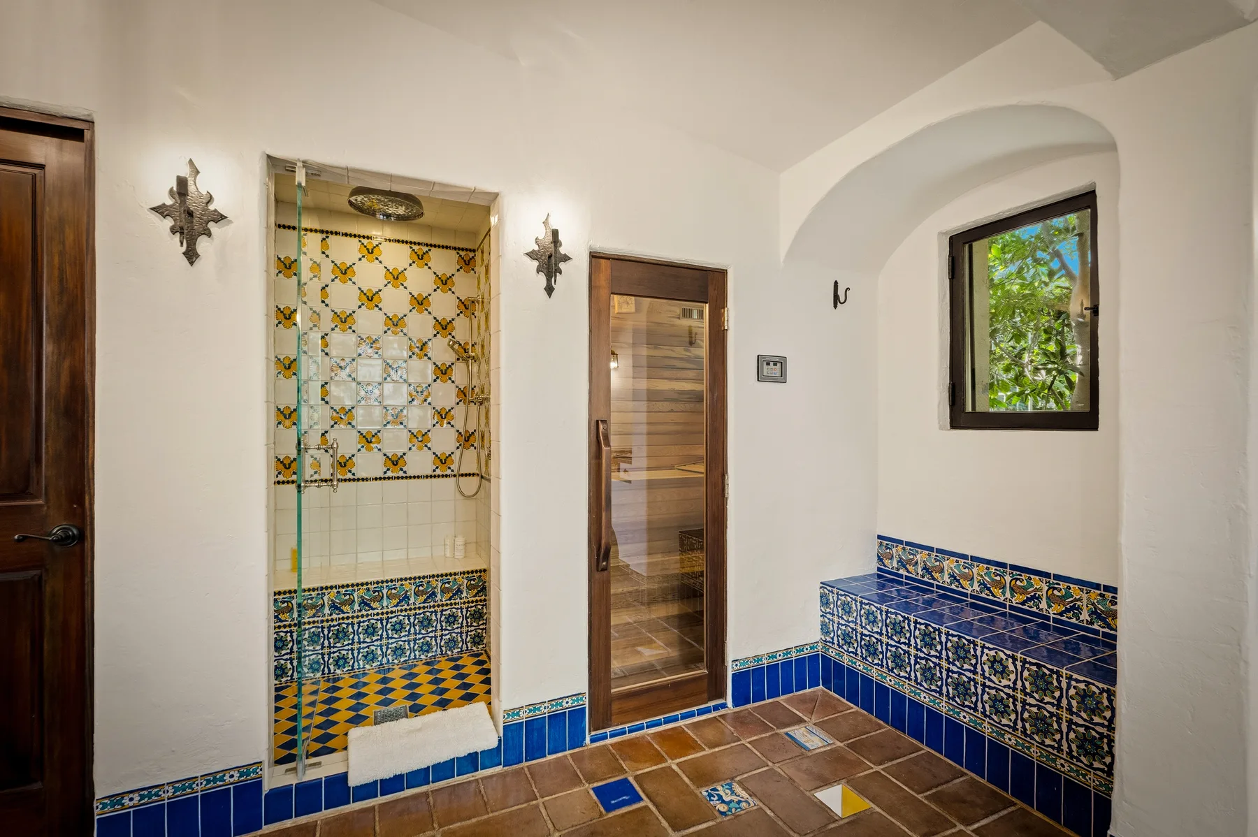 Un baño con azulejos tiene una zona de ducha, una puerta de madera y una ventana pequeña.