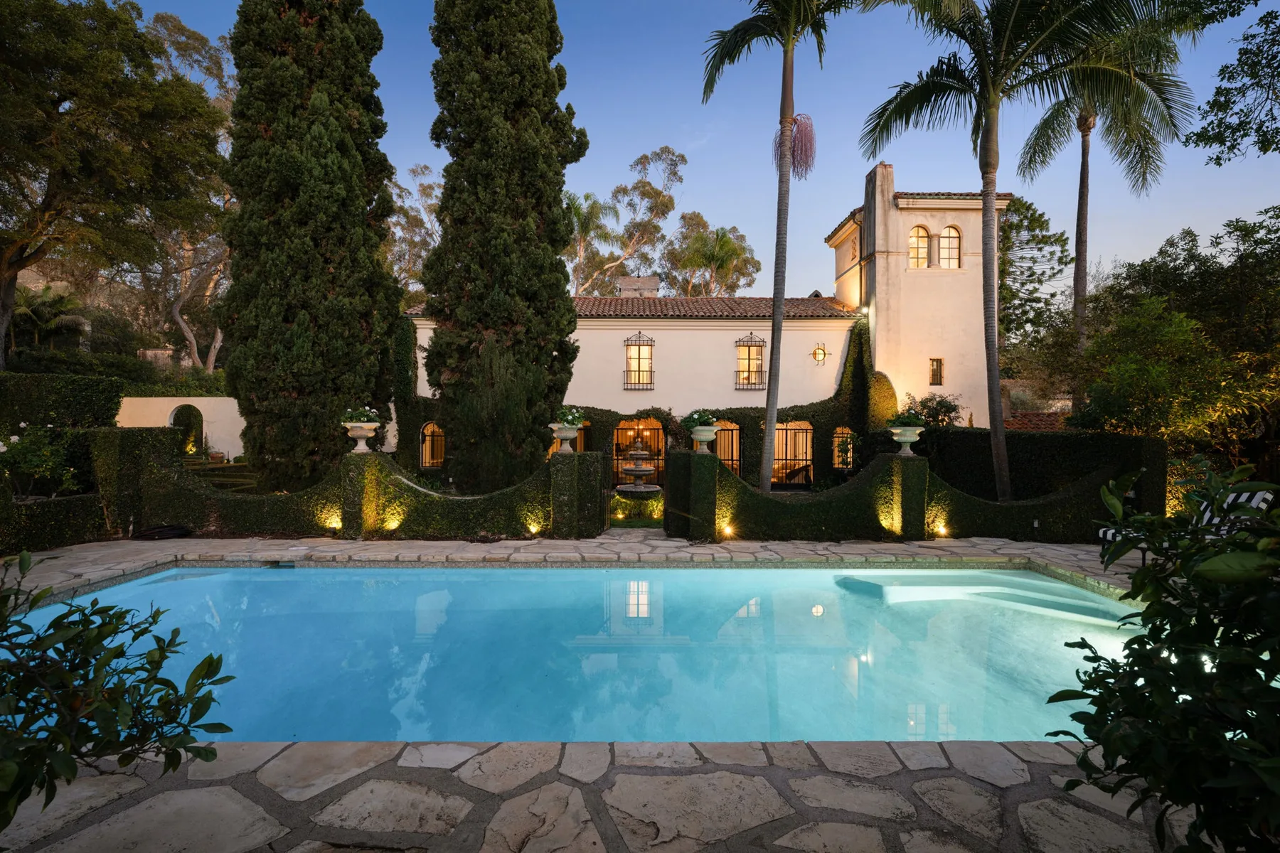 Una piscina está frente a una villa iluminada, rodeada de árboles.